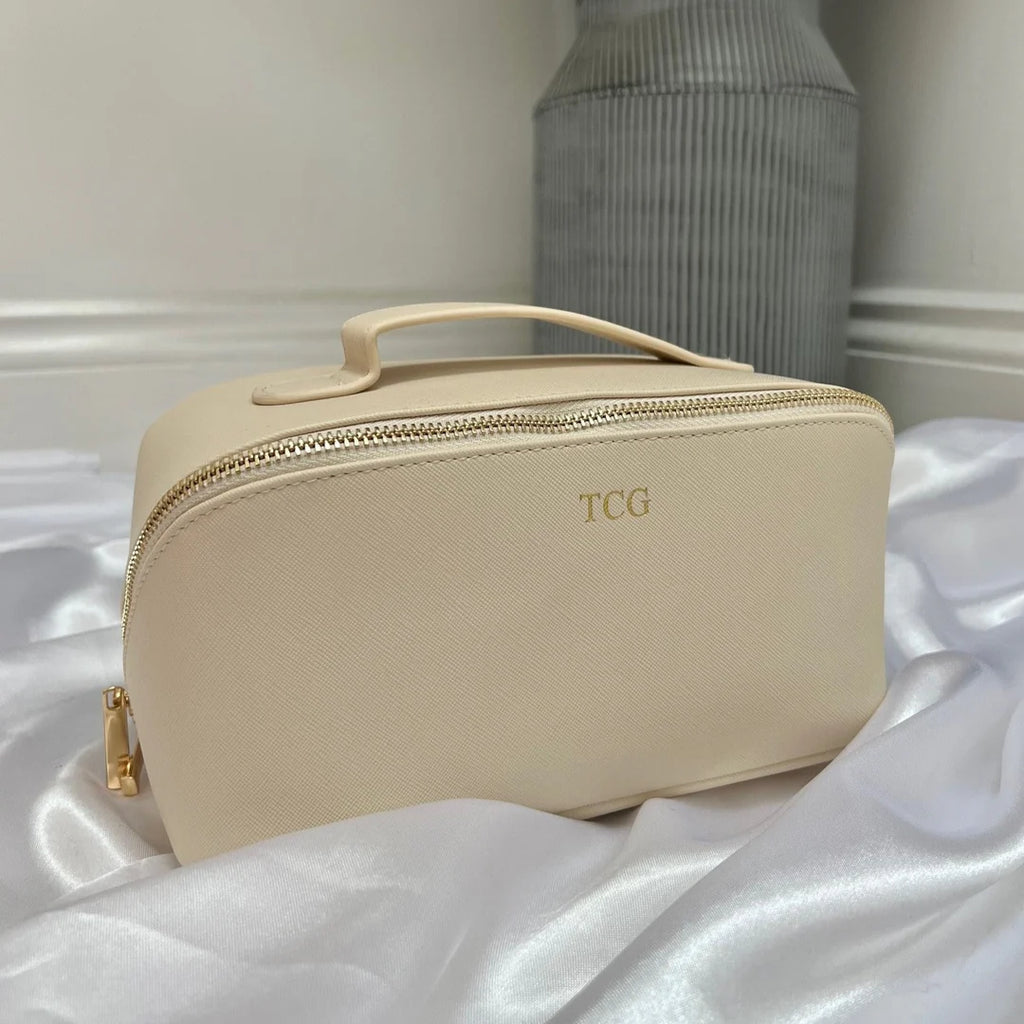 Beige toiletry bag with 'TCG' monogram on a white fabric background