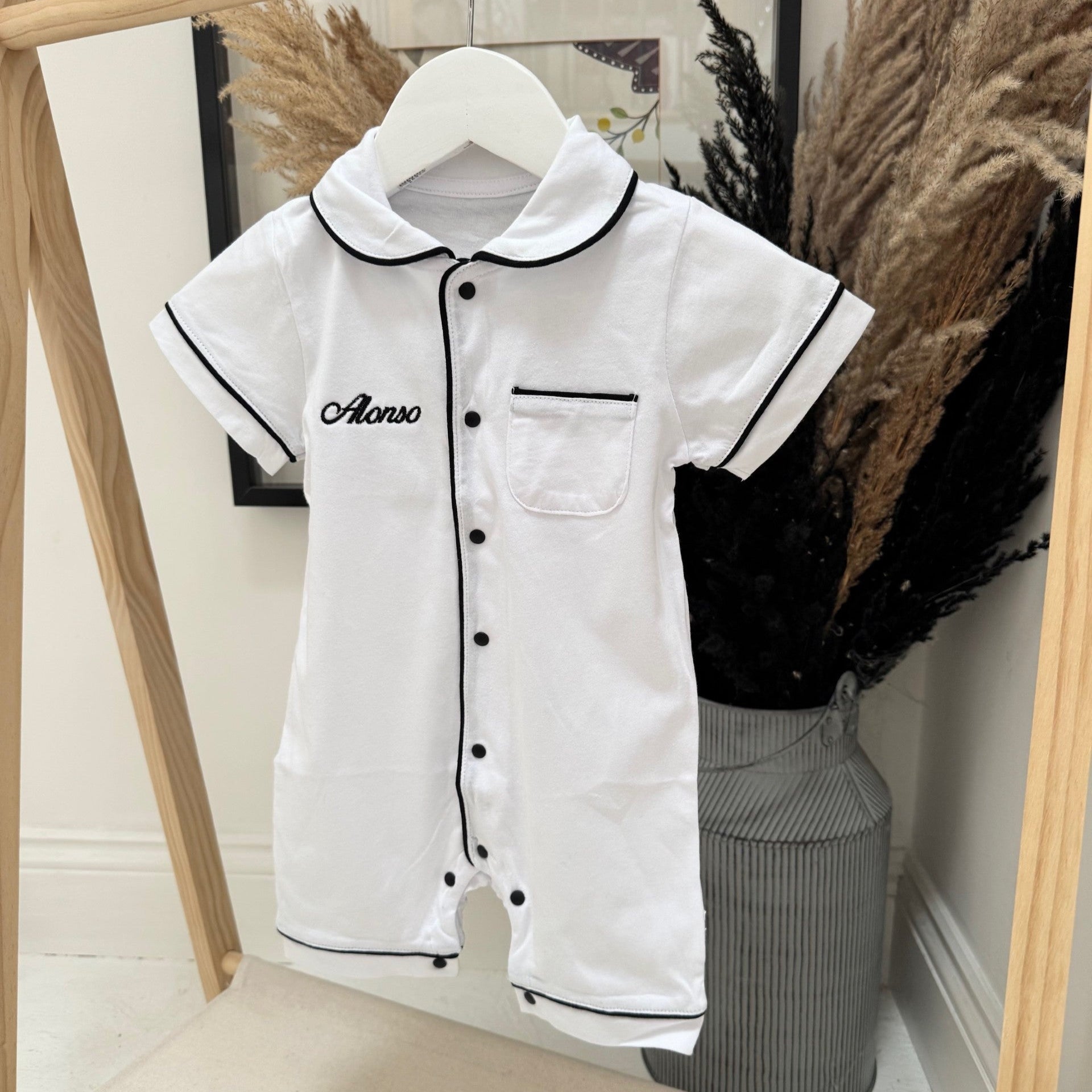 White children's romper with black trim on a hanger against a neutral background