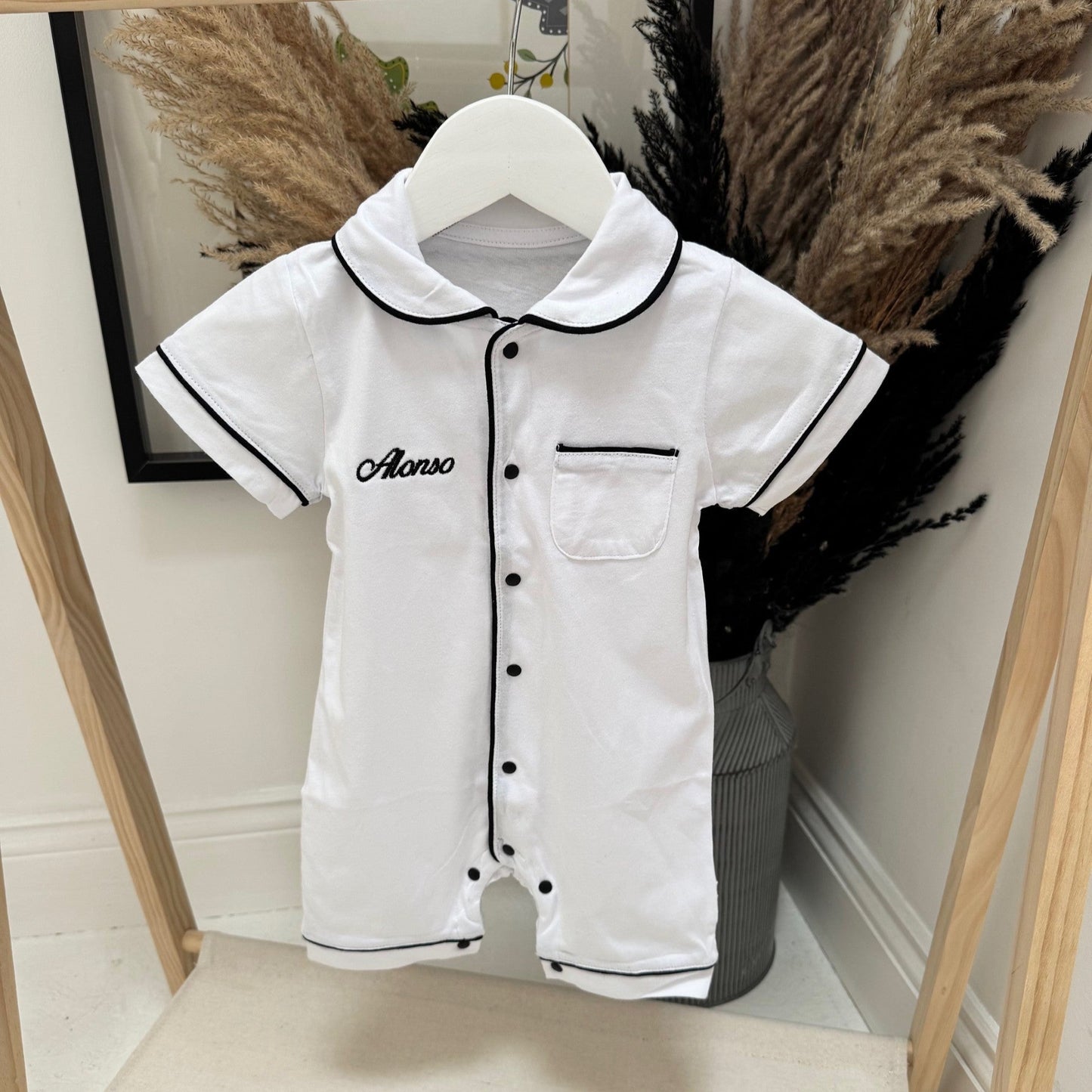 White children's romper with black trim on a hanger against a neutral background