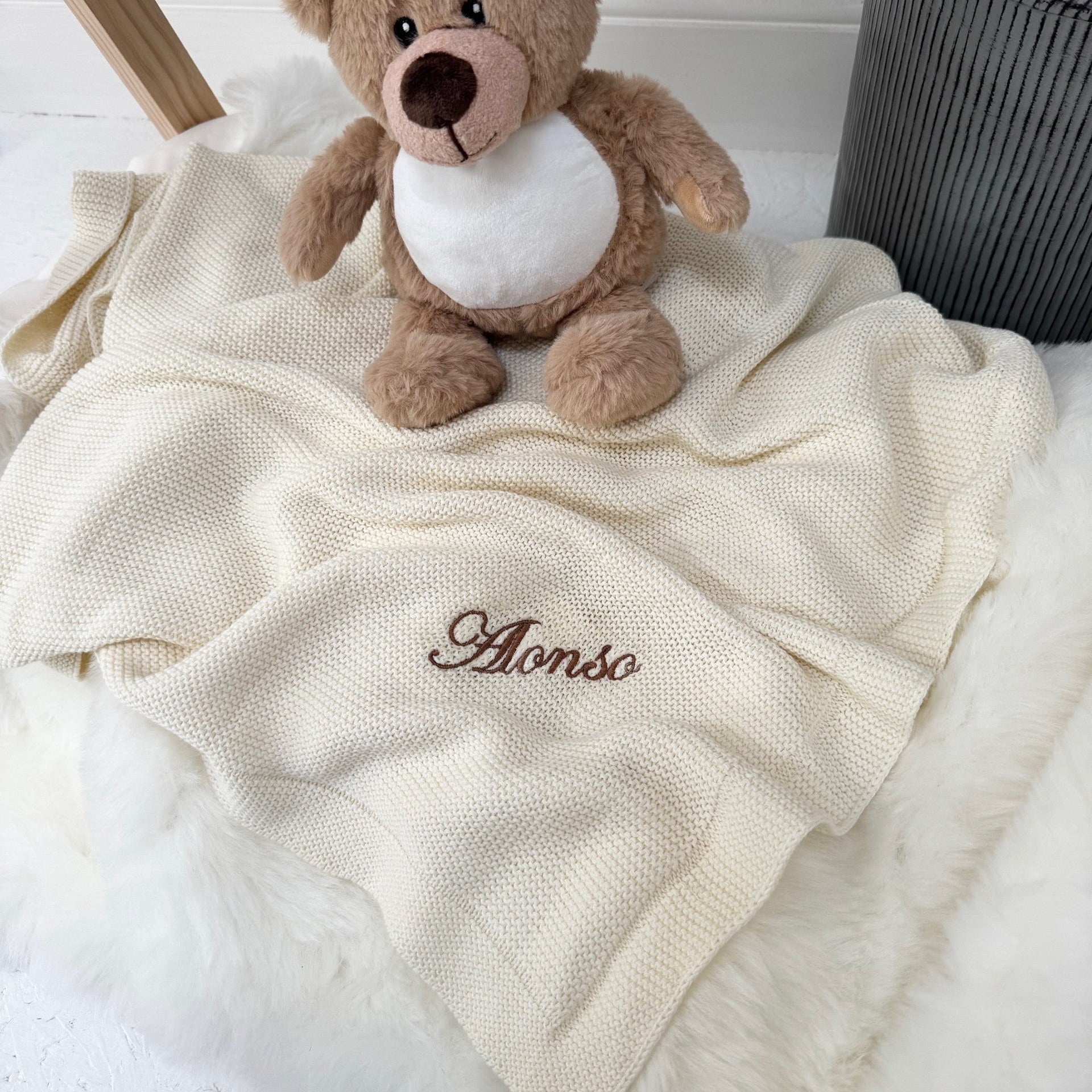 Teddy bear on a white blanket with 'Alonso' embroidered on it, against a light background.