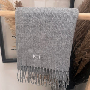 Gray scarf with 'KO' initials on a wooden stick against a neutral background