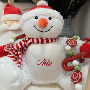 Plush snowman toy with red and white striped scarf, candy cane, and Santa hat.
