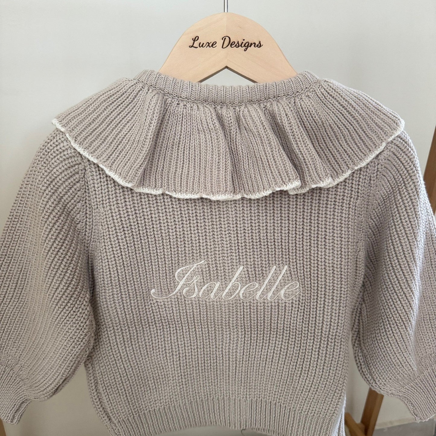 Knitted sweater with ruffled collar and 'Isabelle' embroidery on a hanger.
