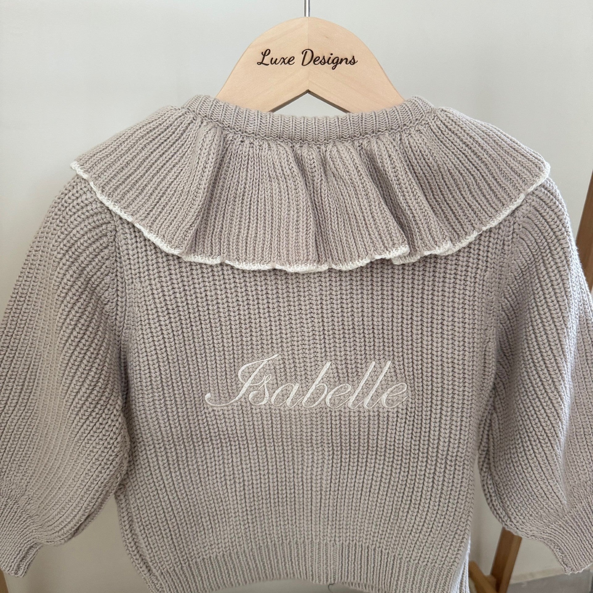 Knitted sweater with ruffled collar and 'Isabelle' embroidery on a hanger.