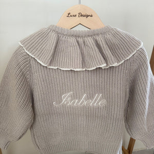 Knitted sweater with ruffled collar and 'Isabelle' embroidery on a hanger.