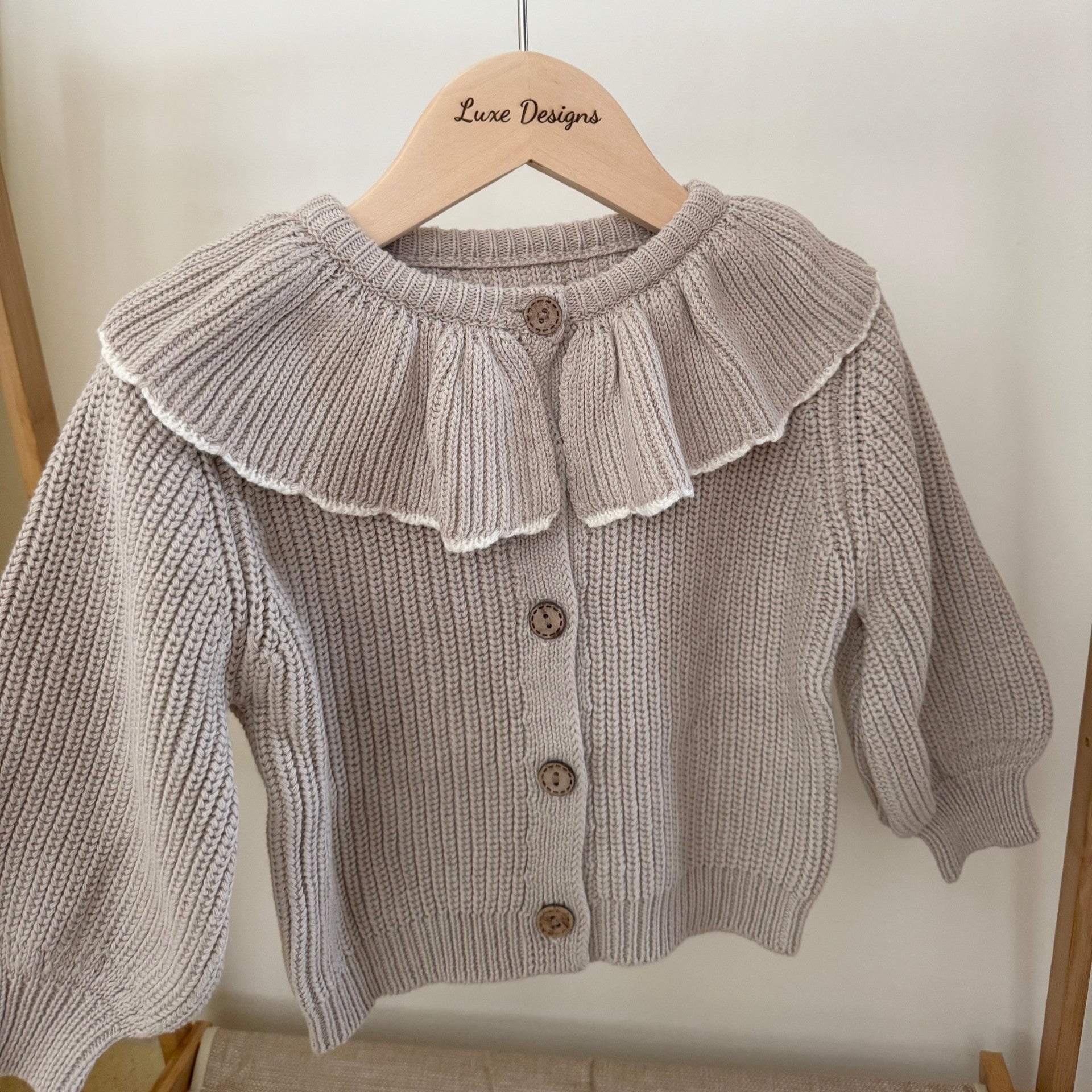 Knitted cardigan with ruffled collar on a hanger against a white background. front of outfit