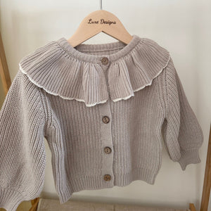Knitted cardigan with ruffled collar on a hanger against a white background. front of outfit