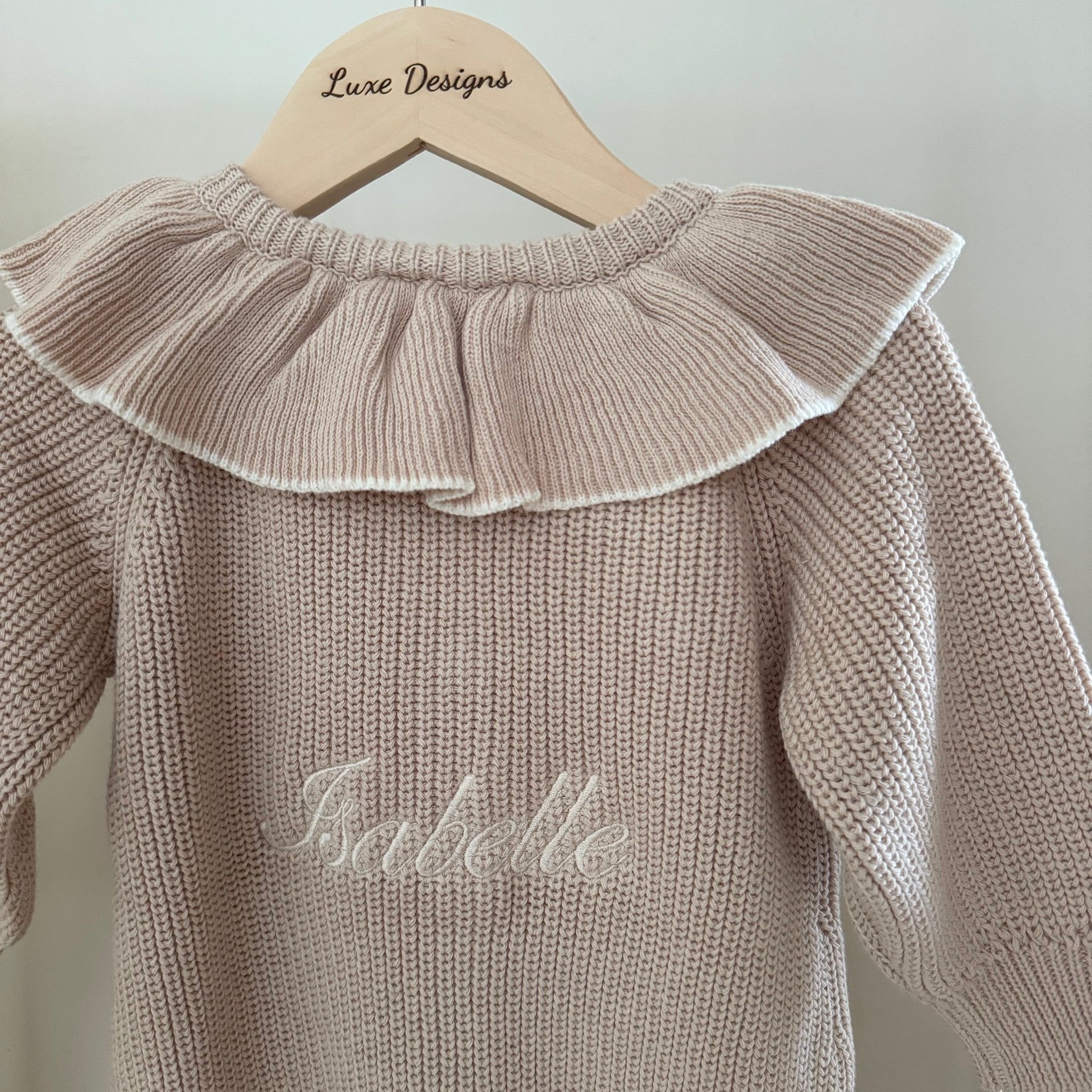 knit romper with ruffled collar and embroidered name on a hanger with 'Luxe Designs' branding.