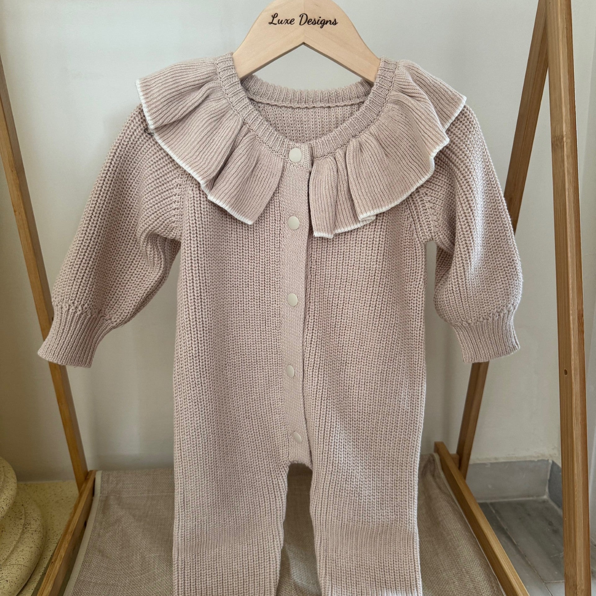 Baby romper with ruffled collar hanging on a wooden rack.
