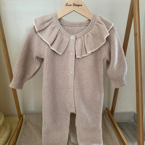 Baby romper with ruffled collar hanging on a wooden rack.