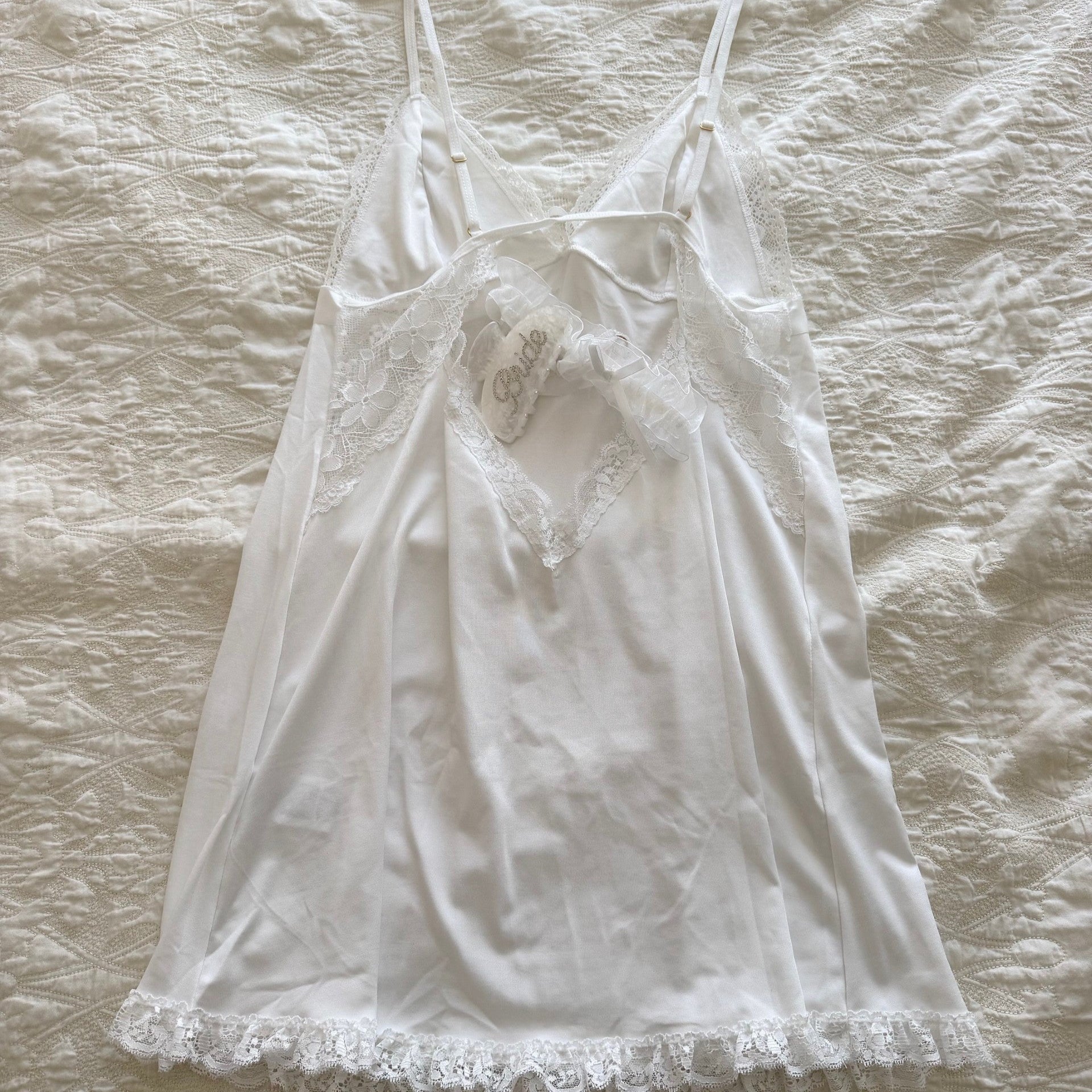White lace-trimmed nightgown on a wooden hanger against a textured beige background