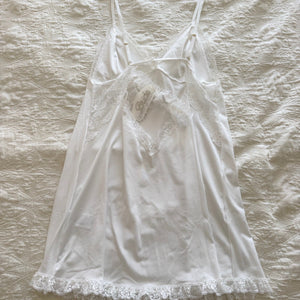 White lace-trimmed nightgown on a wooden hanger against a textured beige background