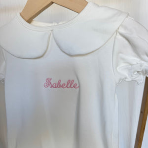 White dress with 'Isabelle' embroidery on a wooden hanger labeled 'Luxe Designs'.