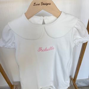 White baby romper with 'Isabelle' embroidered on it, hanging on a wooden hanger with 'Luxe Designs' branding.