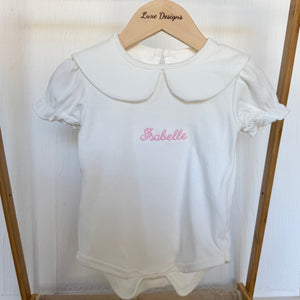 White baby romper with embroidered name on a wooden hanger against a white background
