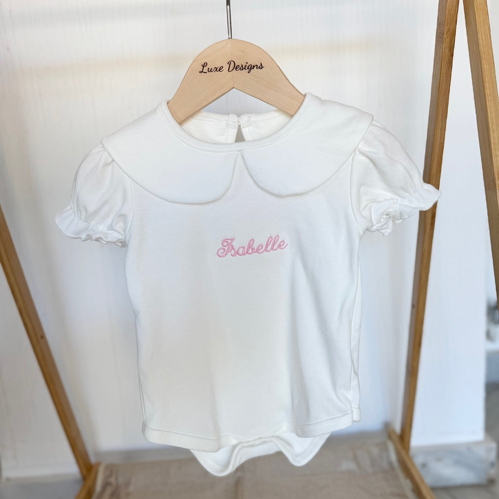 White baby romper with 'Isabelle' embroidered on a wooden hanger against a white background