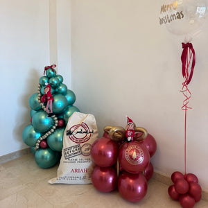 Decorative setup with balloons shaped like a Christmas tree, gift bag, and balloon with 'Happy Christmas' text.