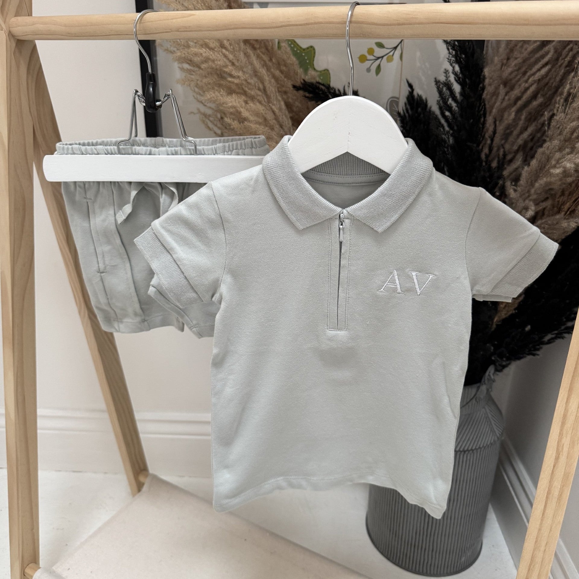 Grey polo shirt with 'AV' logo on a hanger against a neutral background