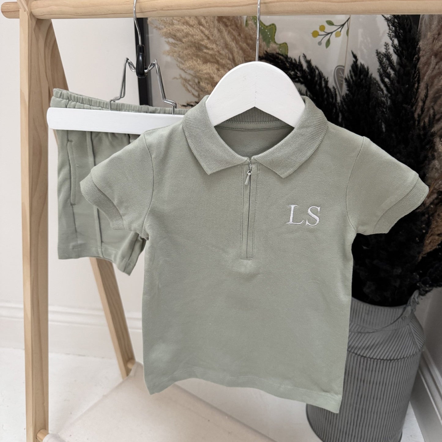 Green polo shirt with 'LS' monogram on a hanger against a neutral background