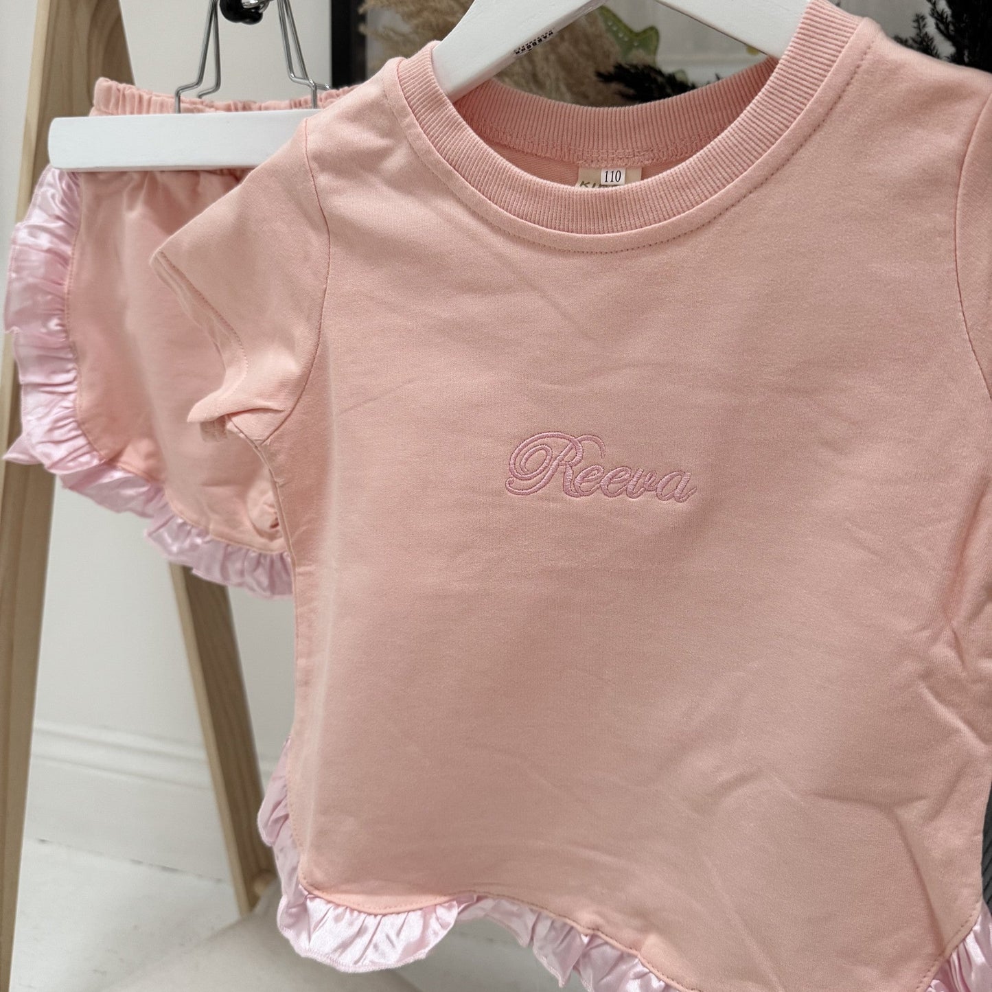 Pink children's outfit with ruffled hem on a hanger.