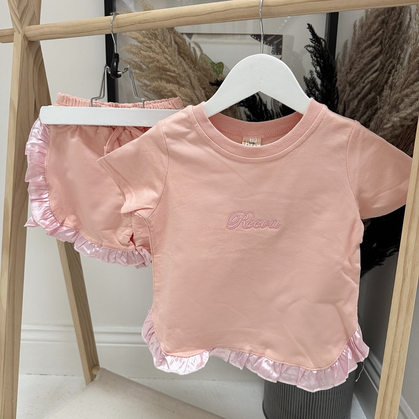 Pink children's top with ruffled sleeves on a hanger against a neutral background