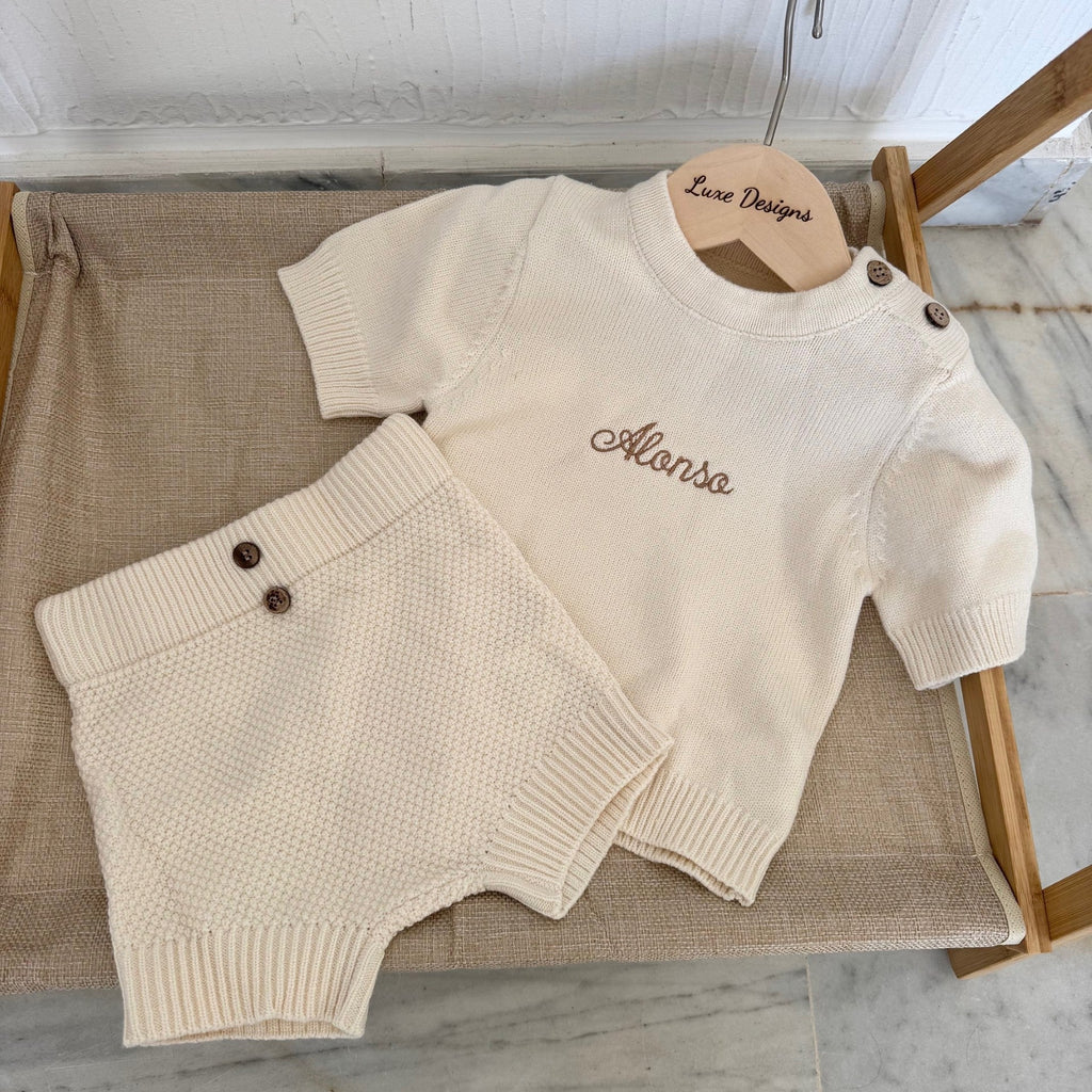 Beige sweater and shorts set on a wooden hanger with 'Alonso' embroidered on it, placed on a textured surface.