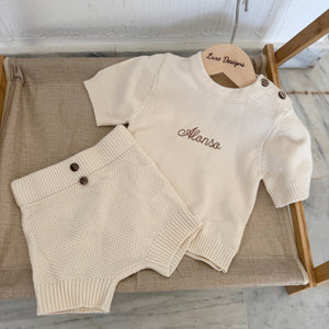 Beige sweater and shorts set on a wooden hanger with 'Alonso' embroidered on it, placed on a textured surface.