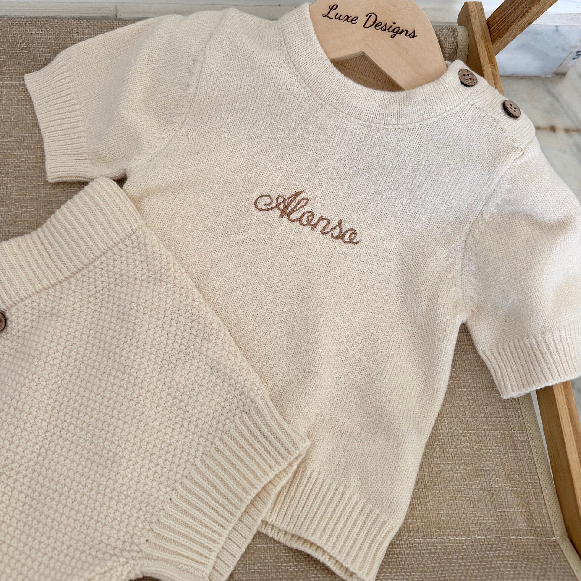 Beige baby sweater set with 'Alonso' embroidery on a wooden hanger.