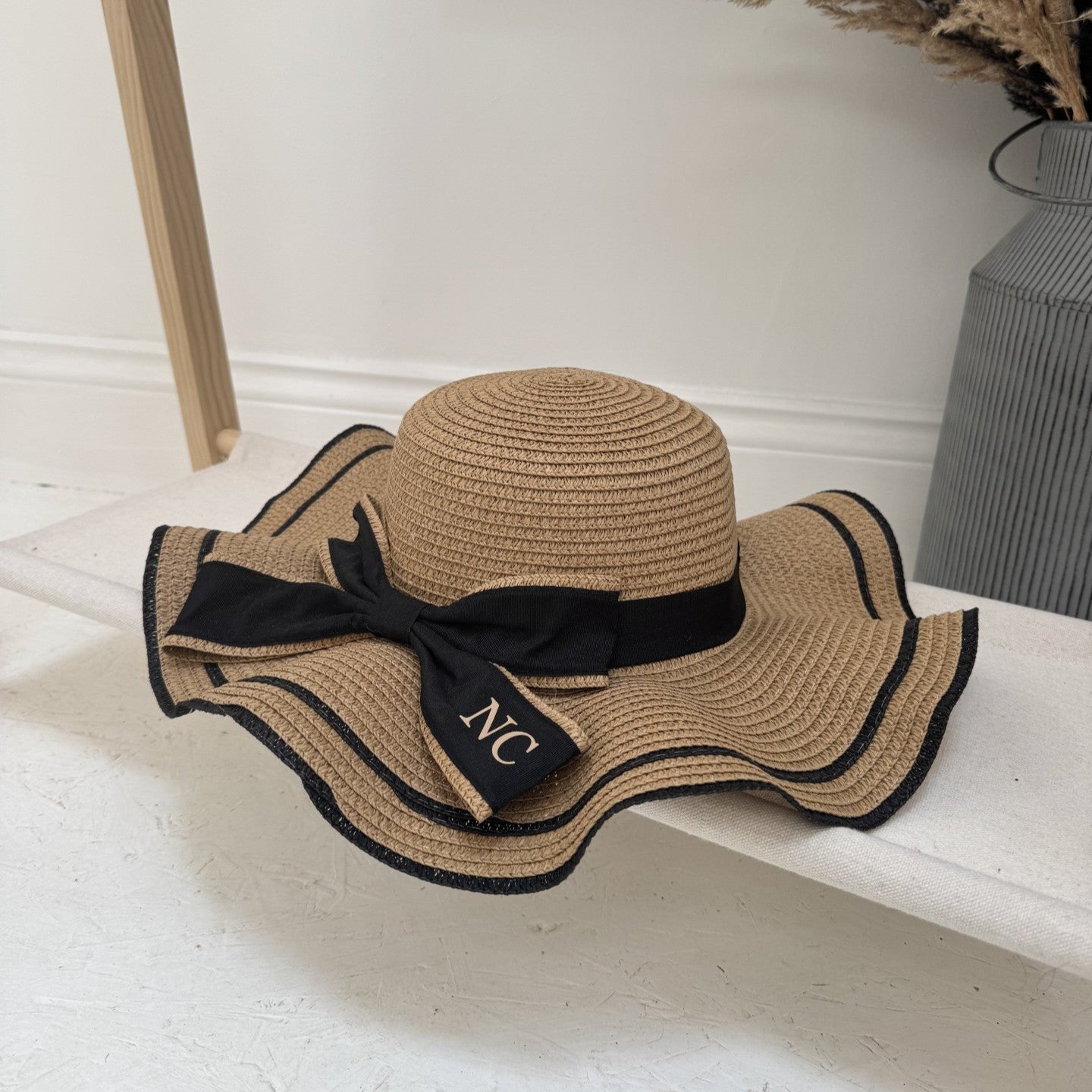 Brown straw hat with black ribbon and 'NC' initials on a white surface.