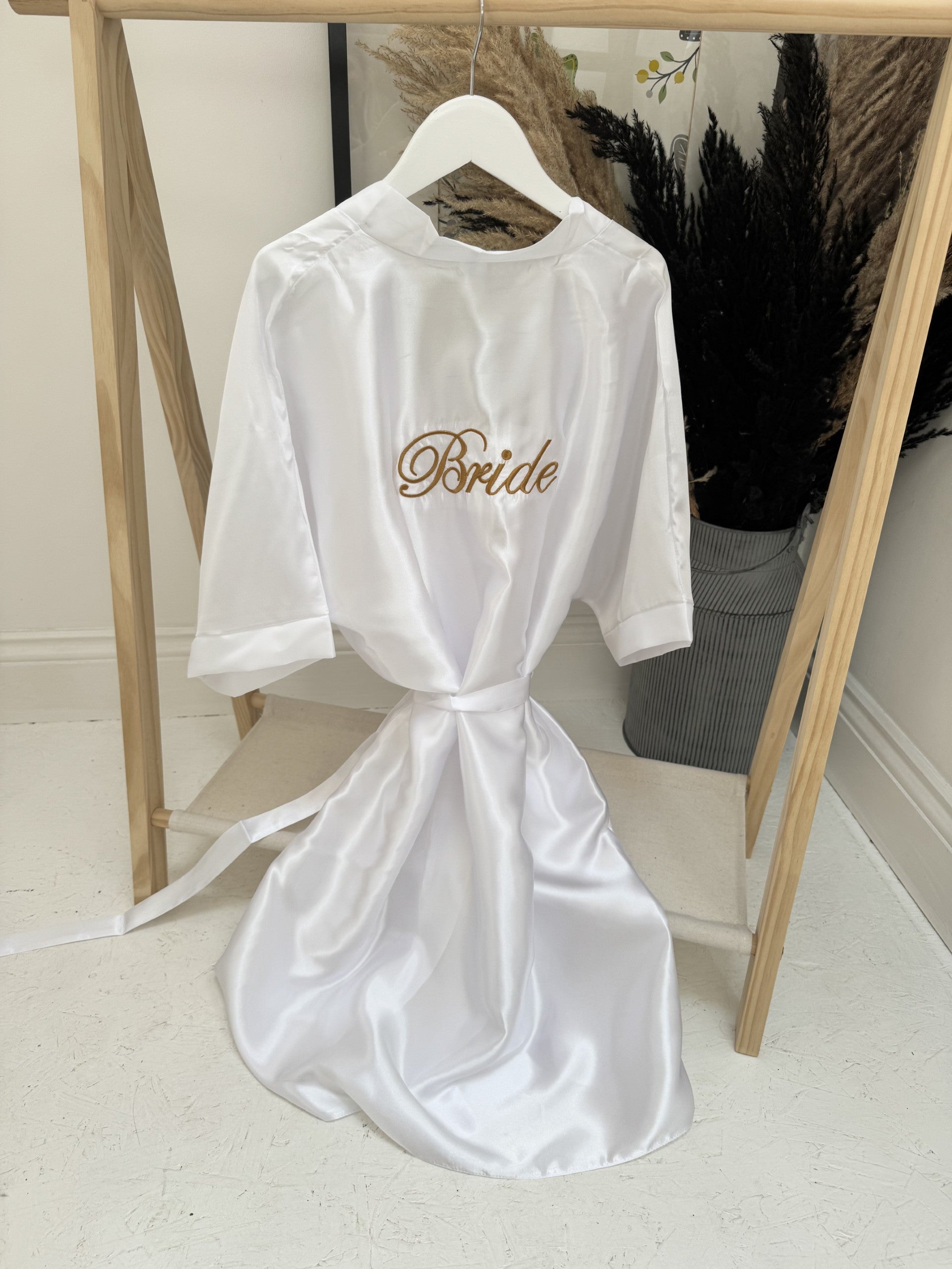 White satin robe with 'Bride' embroidery on a hanger against a neutral background