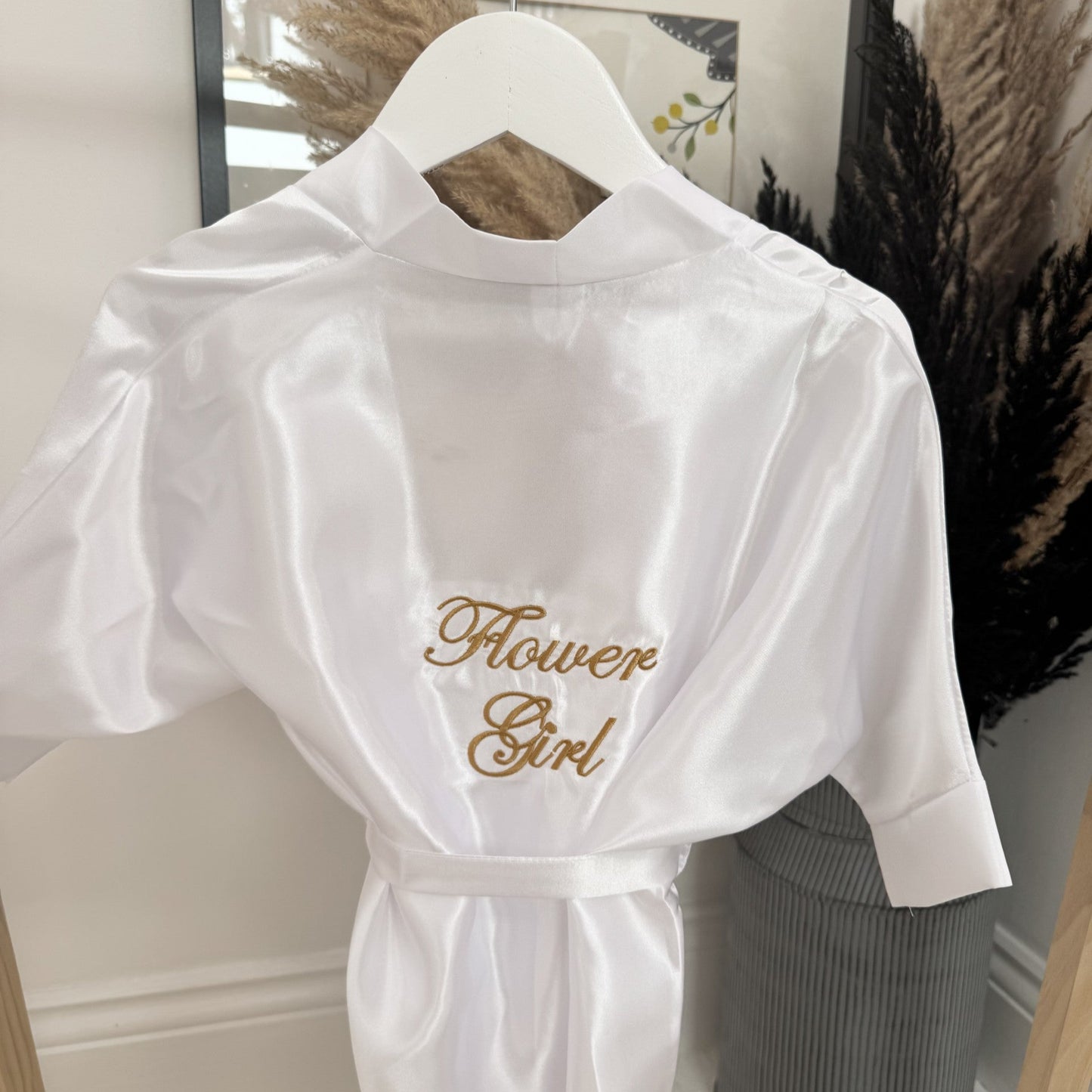 White robe with 'Flower Girl' embroidery on a hanger against a neutral background