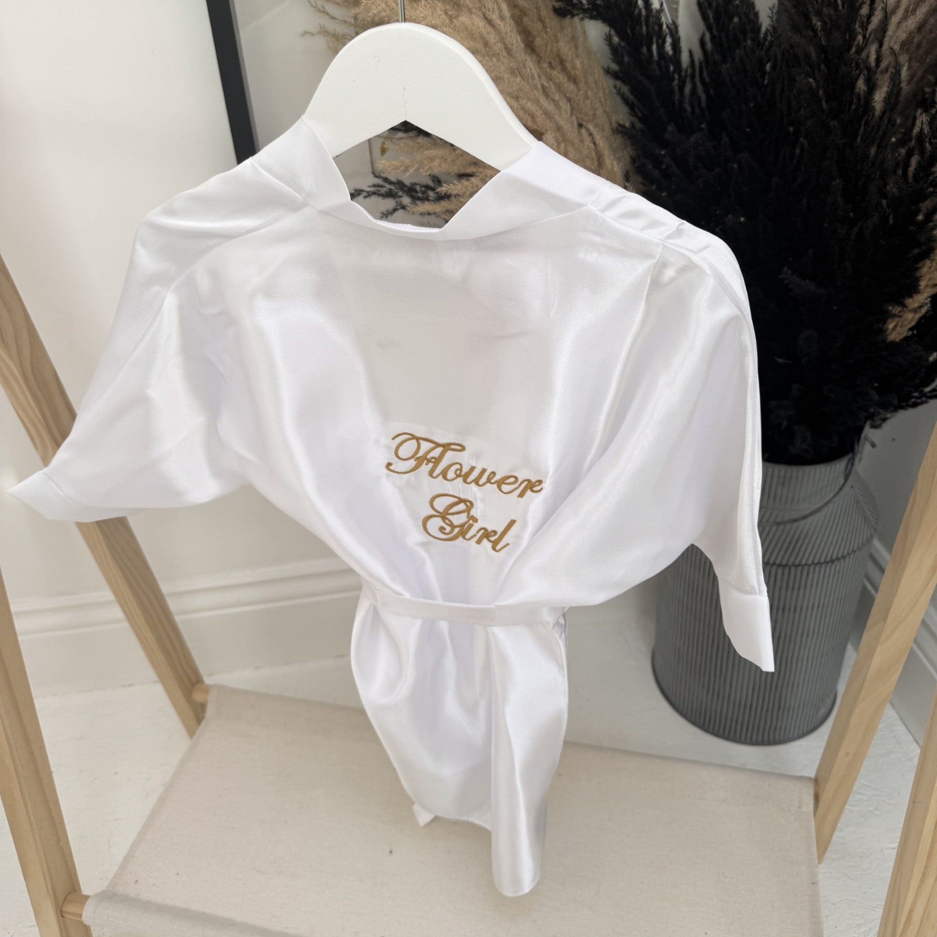 White shirt with 'Flower Girl' embroidery on a hanger against a neutral background