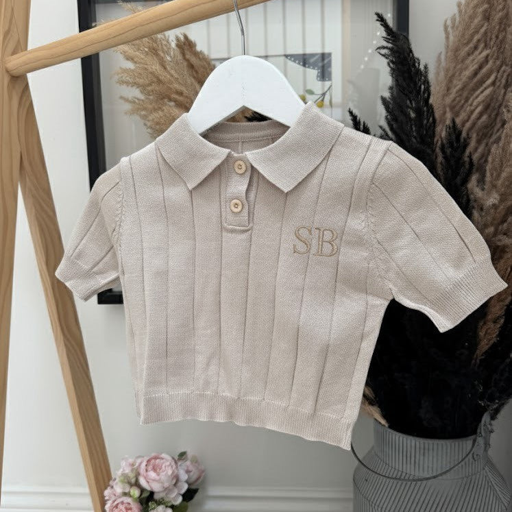 Beige polo shirt with 'SB' monogram on a hanger against a neutral background