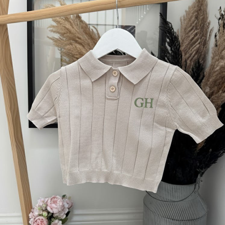 Beige ribbed polo shirt with 'GH' monogram on a hanger against a white wall.