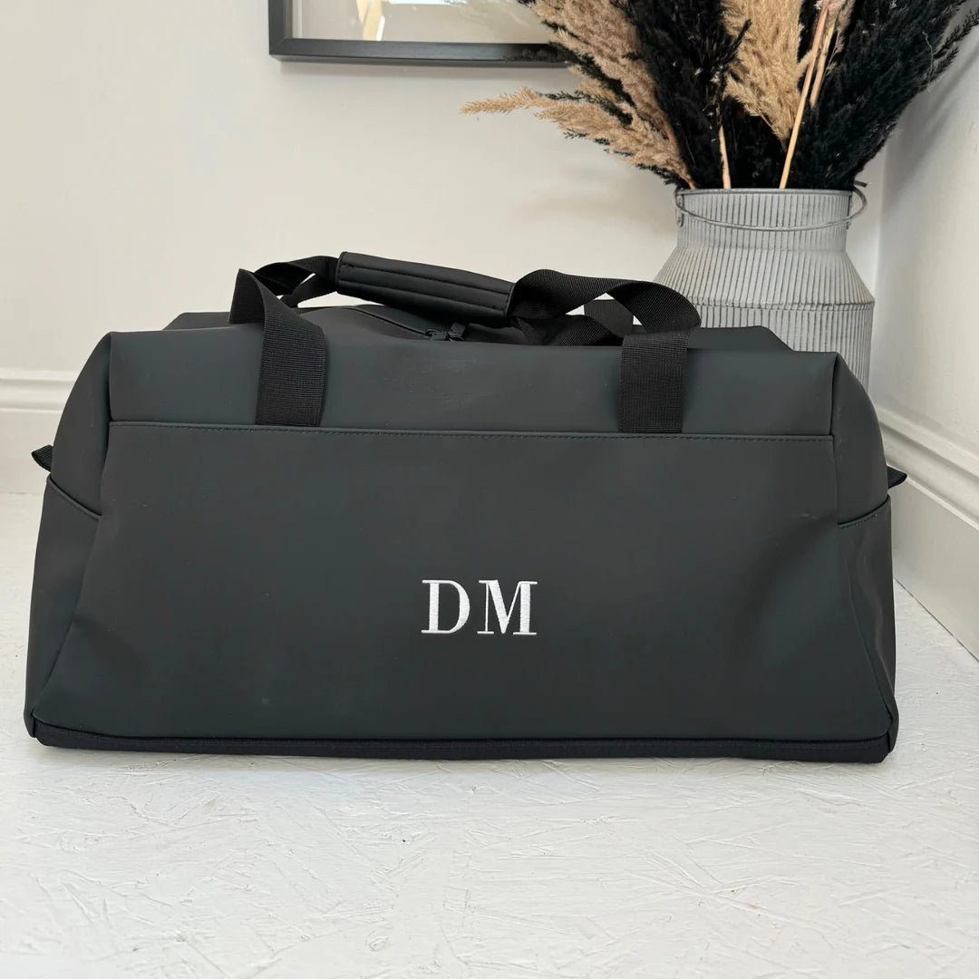 Black duffel bag with 'DM' initials on a light wooden floor.
