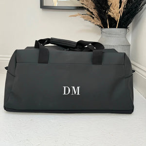 Black duffel bag with 'DM' initials on a light wooden floor.