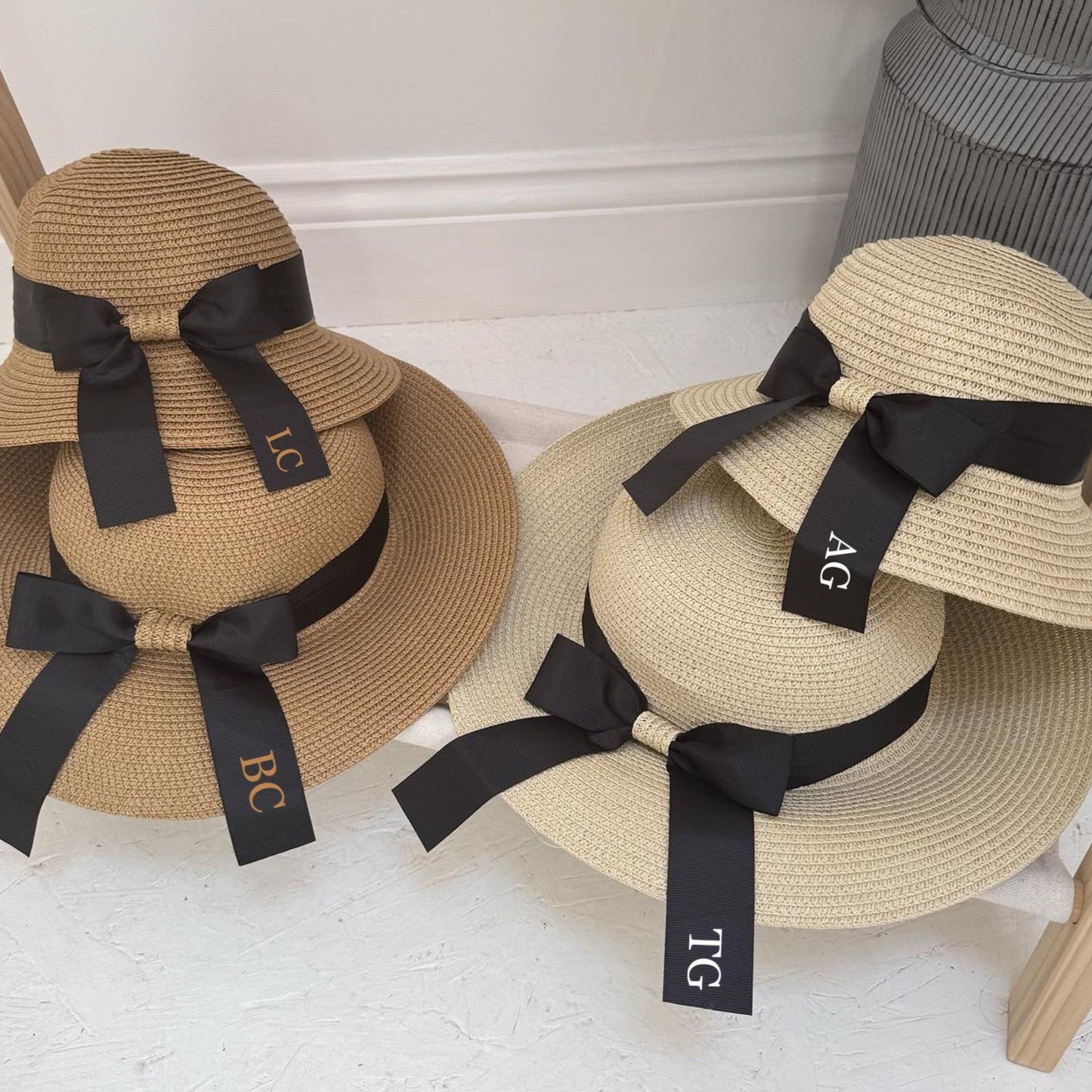 Two straw hats with black ribbons and monogram labels on a white surface.