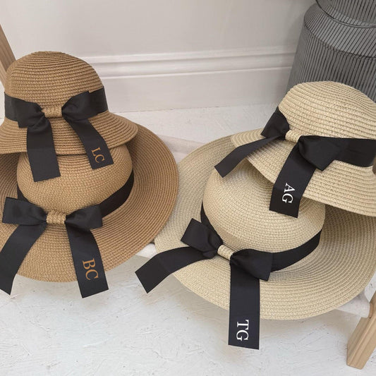 Two straw hats with black ribbons and monogram labels on a white surface.