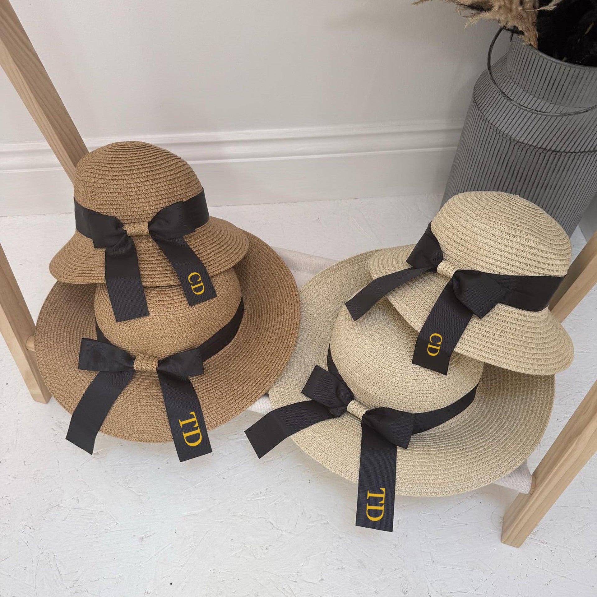 Four straw hats with black ribbons and personalised initials on a white surface.