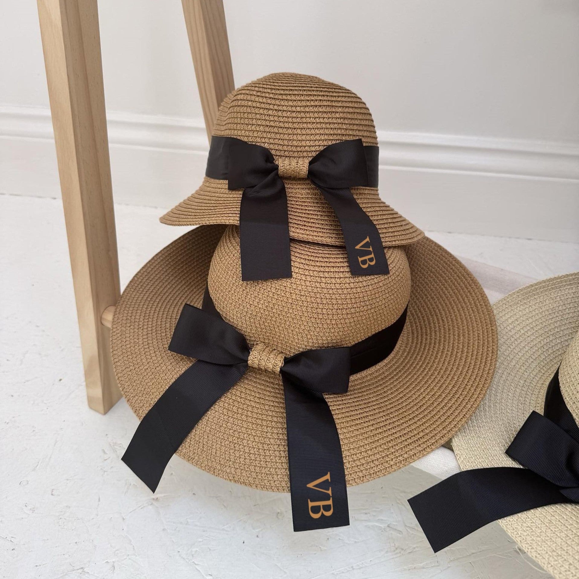 Straw hats with black ribbons and 'VB' monogram on a white floor.