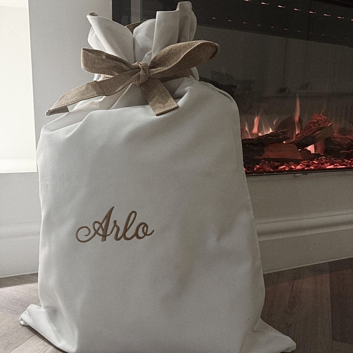 White gift bag with 'Arlo' embroidered on it in front of a fireplace.