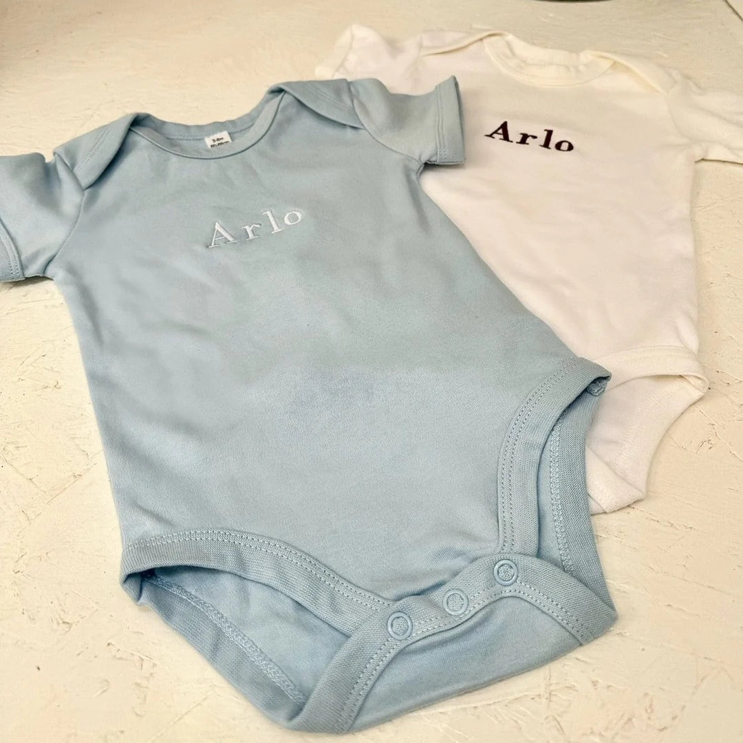 Light blue and white baby onesies with 'Arlo' embroidered on it