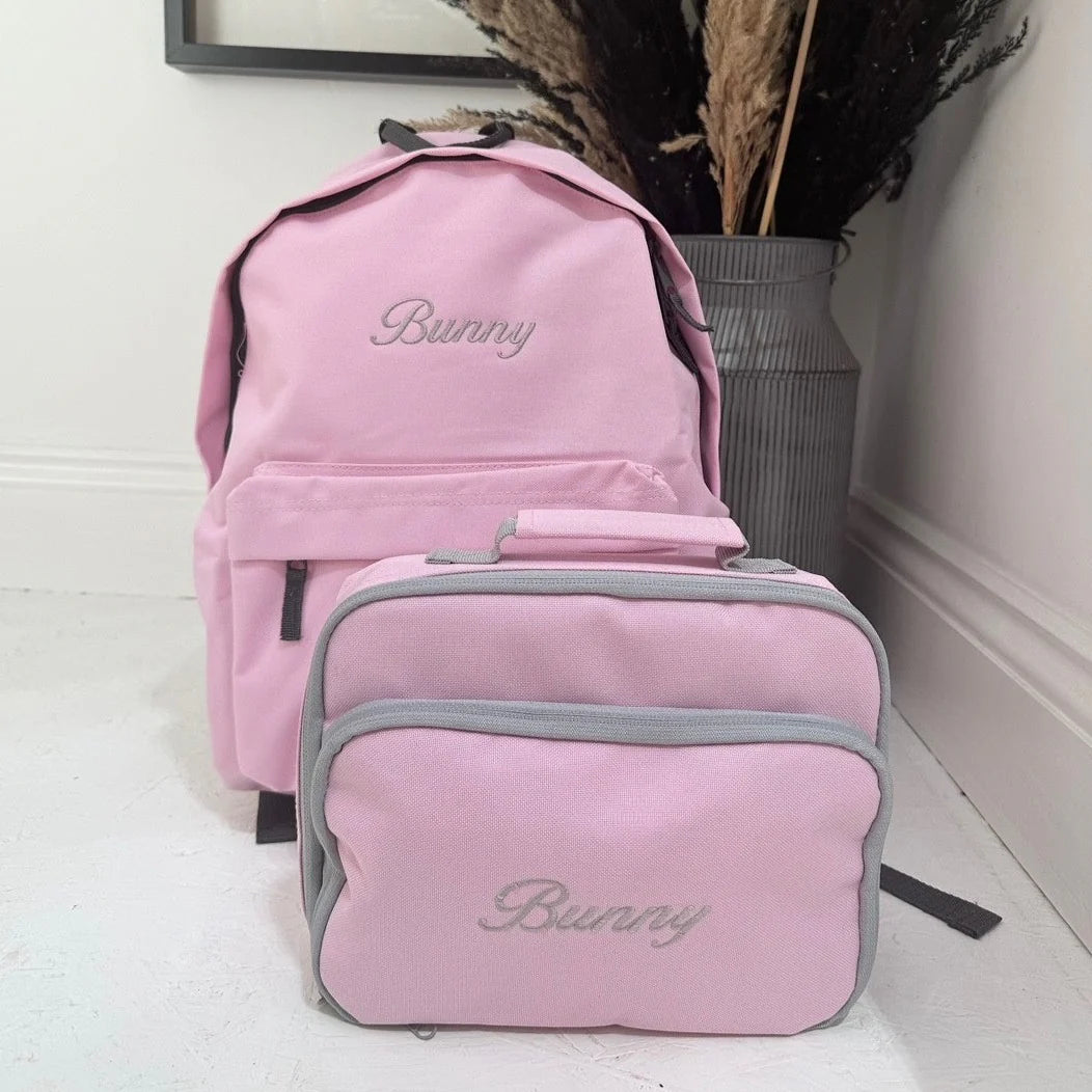 Pink backpack and lunch bag set with 'Bunny' embroidery on a light wooden floor.