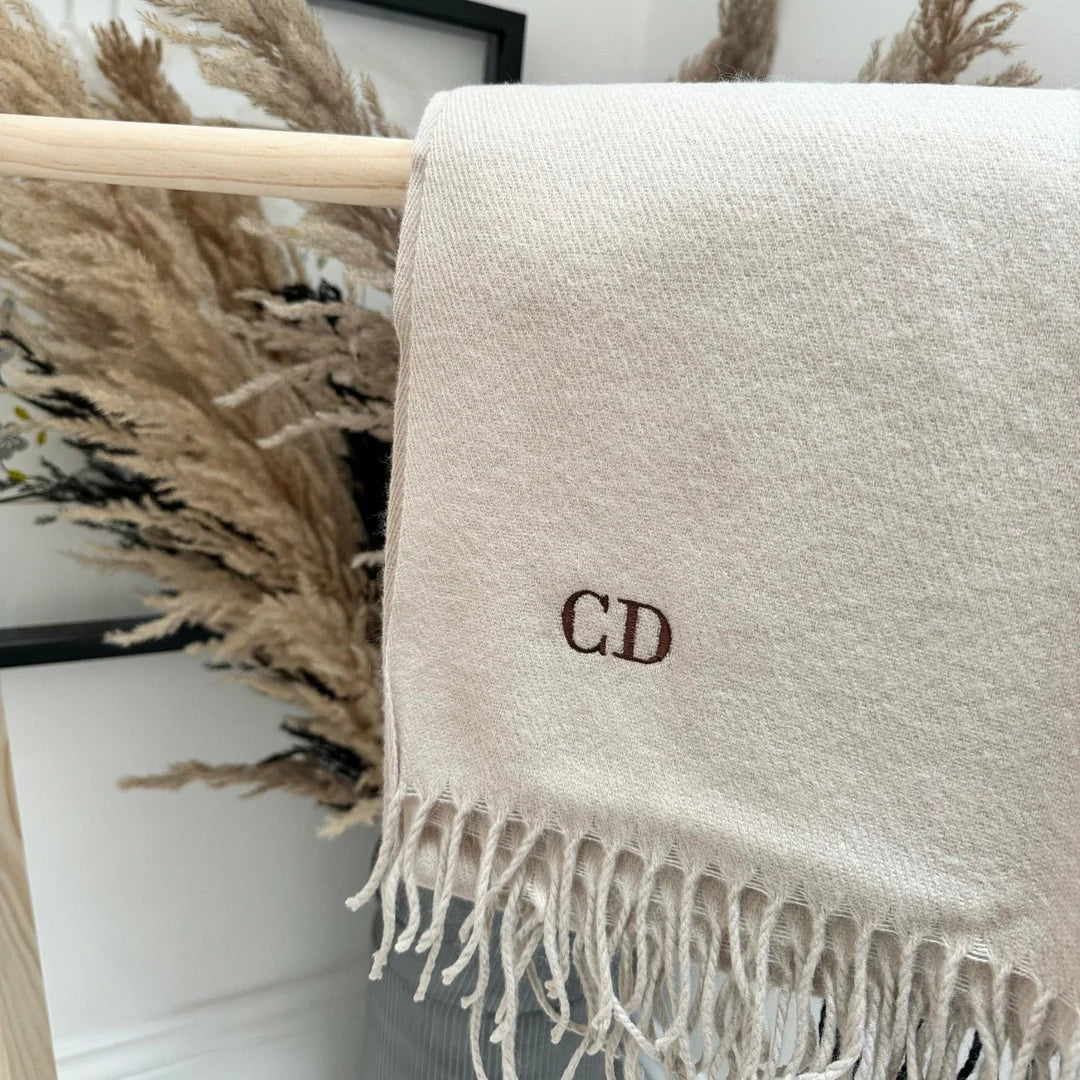 Beige scarf with initials 'CD' draped over a wooden rack with decorative elements in the background.