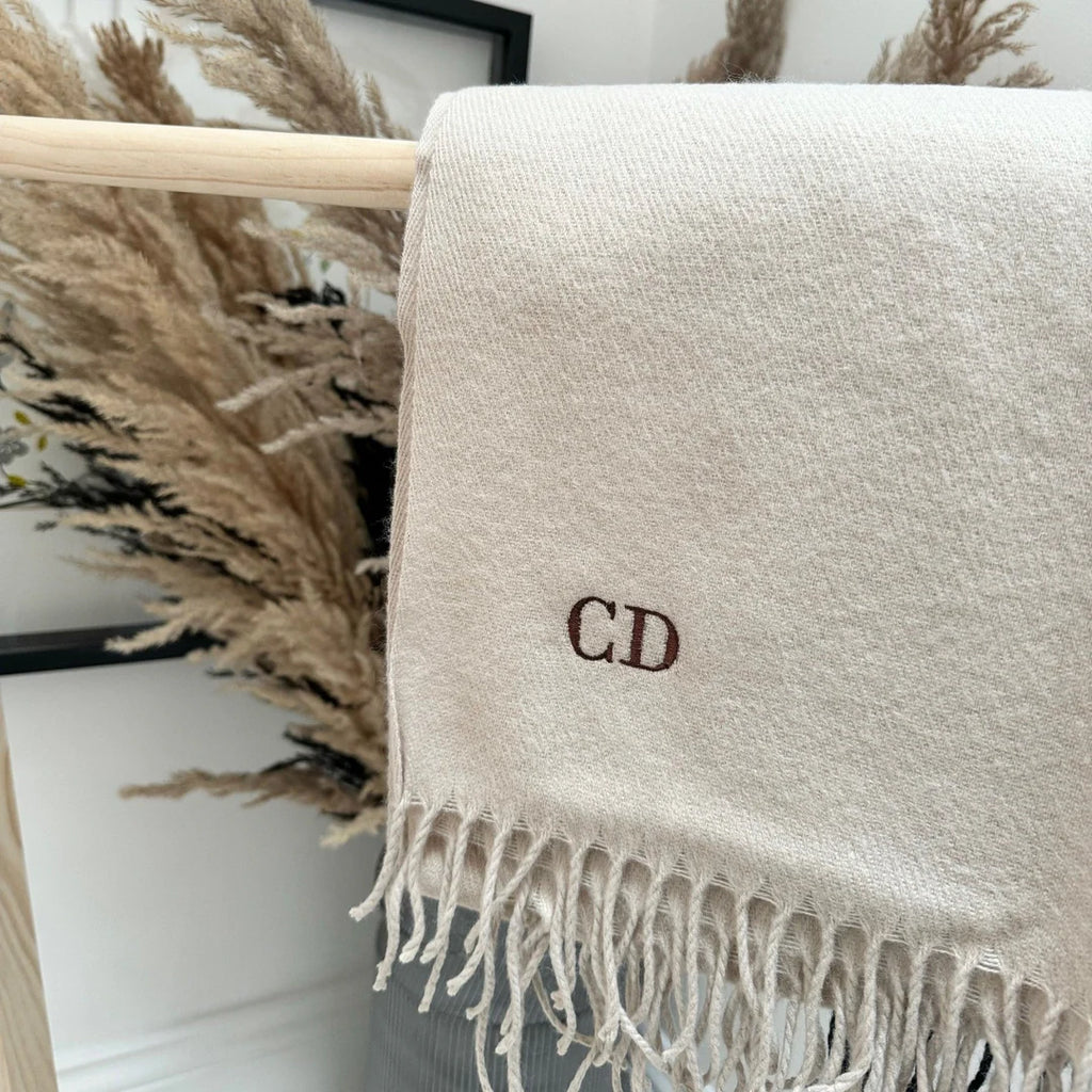 Beige scarf with initials 'CD' draped over a wooden rack with decorative elements in the background.