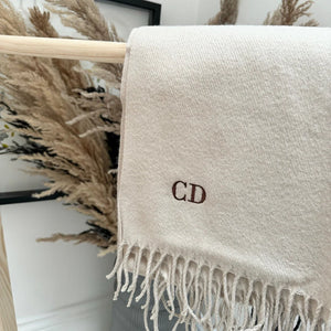 Beige scarf with initials 'CD' draped over a wooden rack with decorative elements in the background.
