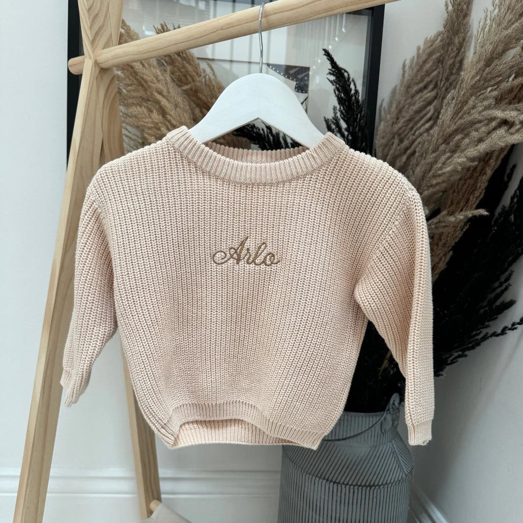Beige knit sweater with 'Arlo' embroidery on a hanger against a neutral background