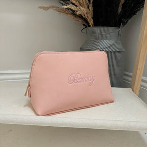 Pink pouch with 'Bunny' branding on a white surface with a vase in the background