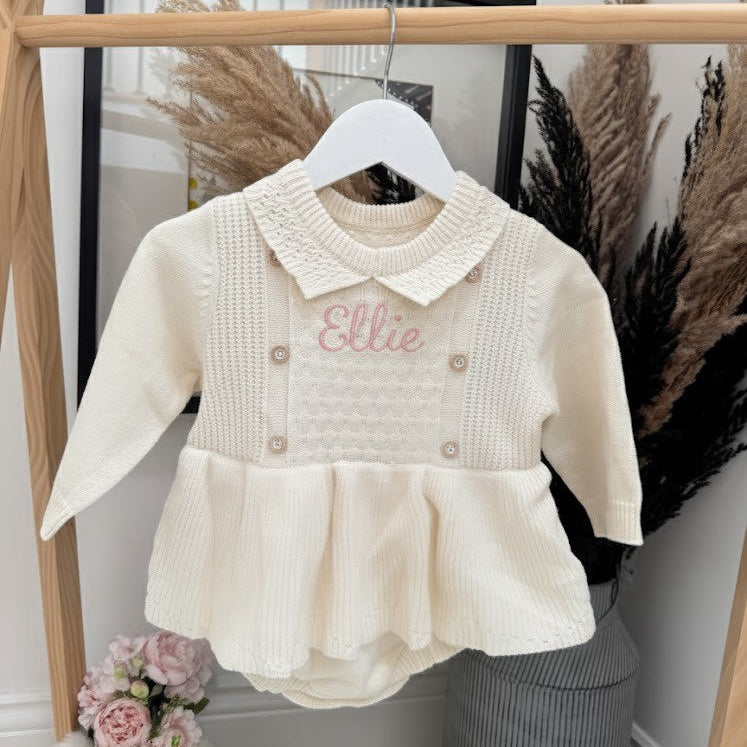 Baby outfit with embroidered name on a hanger against a neutral background
