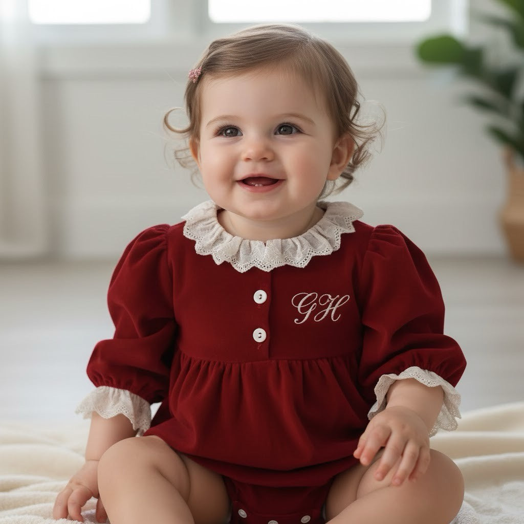 close up of baby sat on floor in a red romper with her initials on
